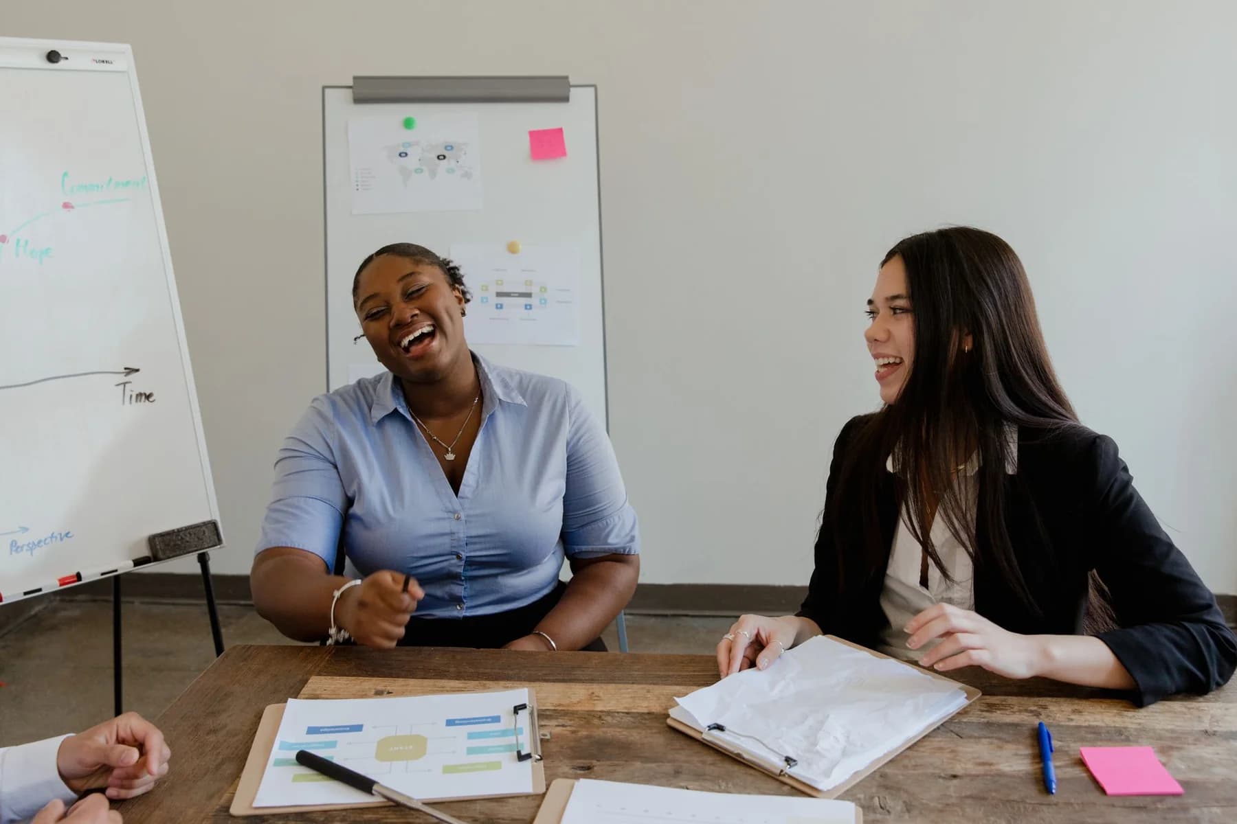 Twee vrouwen lachen tijdens een gesprek aan een werktafel.